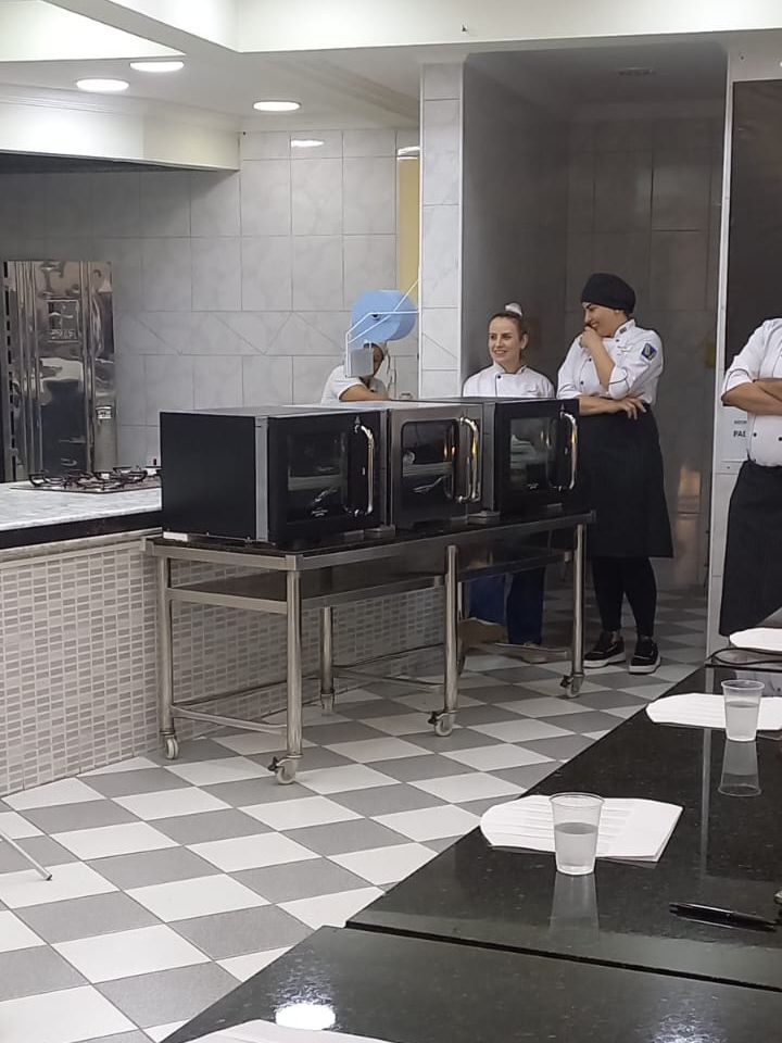 Um grupo de pessoas está em pé ao redor de uma mesa em uma cozinha