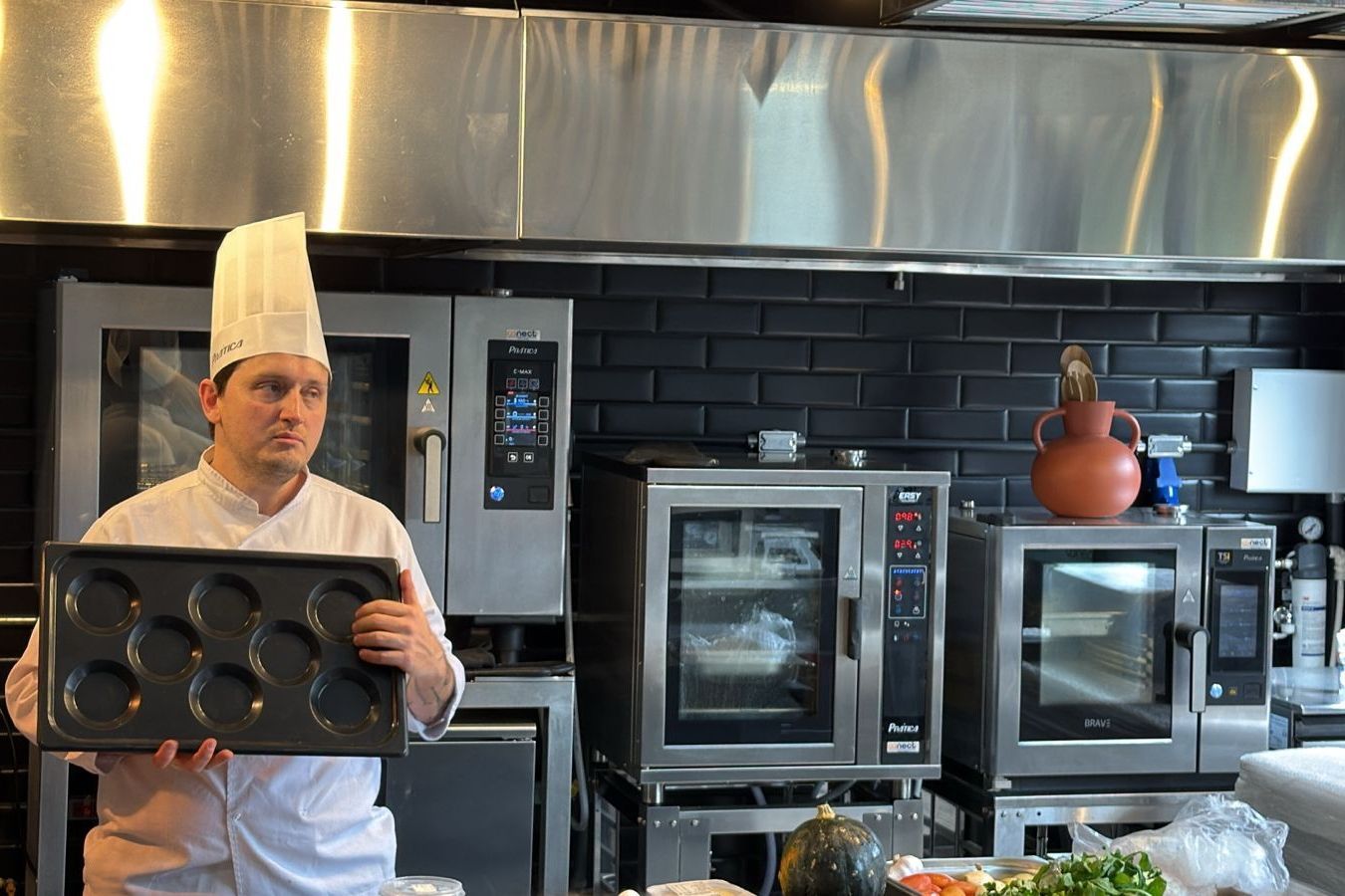 Chef segurando uma forma de muffin em uma cozinha comercial com fornos.