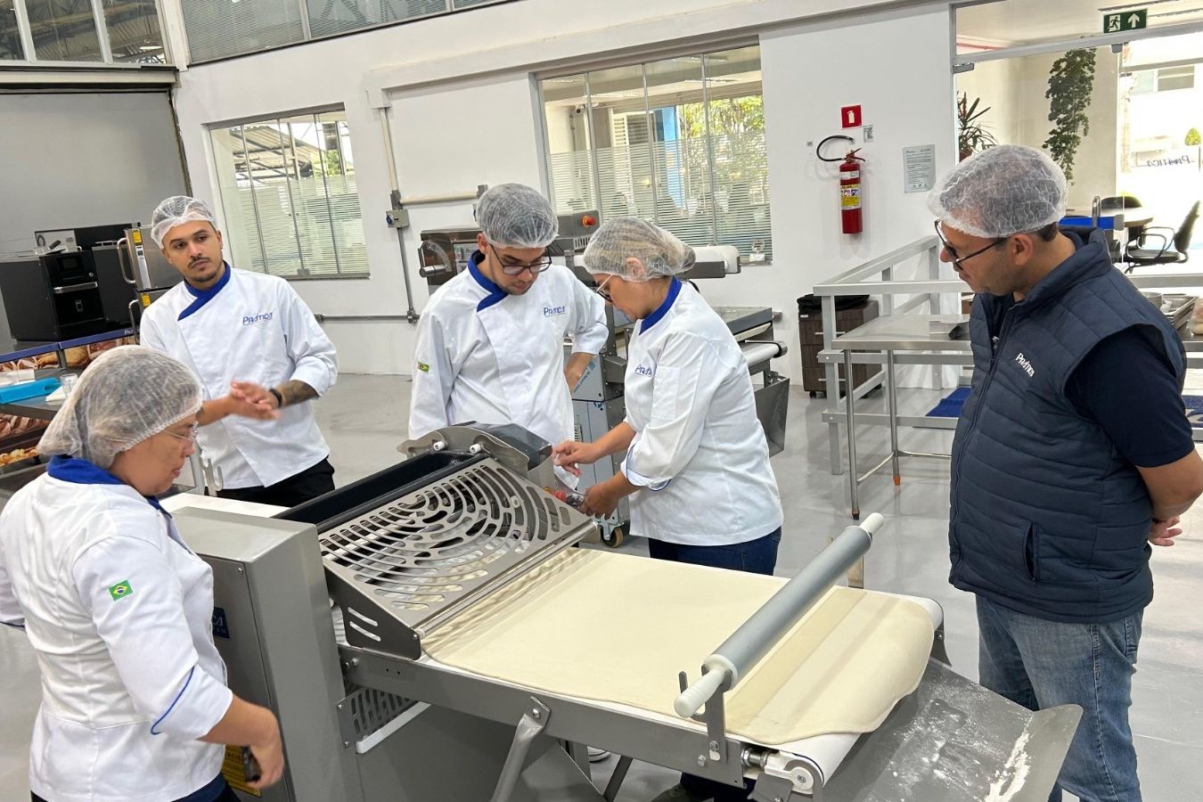 Pessoas em jalecos de chef inspecionando a massa em uma máquina em uma padaria.