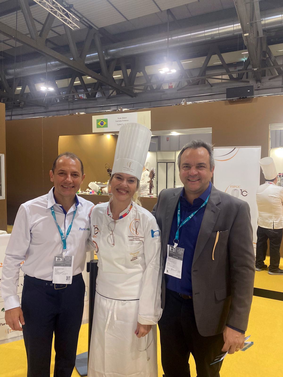 Uma mulher com um chapéu de chef está posando para uma foto com dois homens.