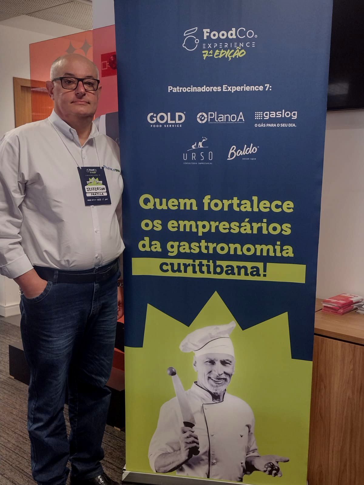 A man standing next to a sign that says quem fortalece os empresarios da gastronomia curitibana