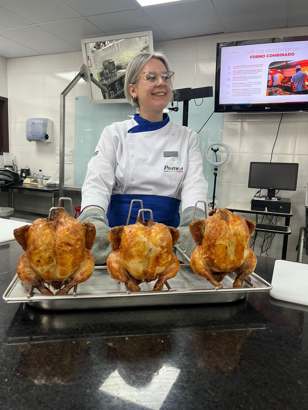 Uma mulher está parada em frente a uma bandeja de frangos assados.