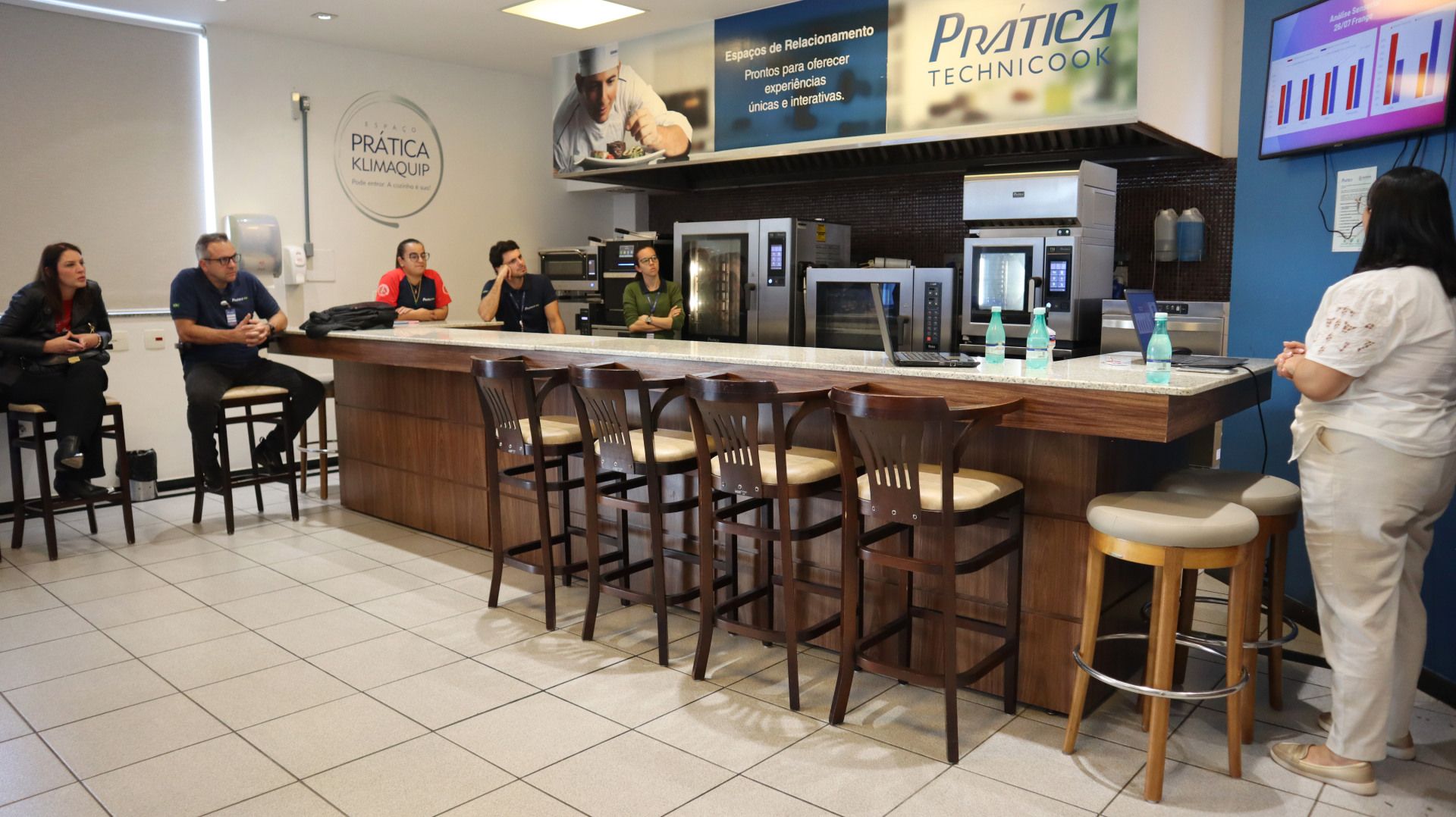 Um grupo de pessoas está sentado em um longo balcão na cozinha.