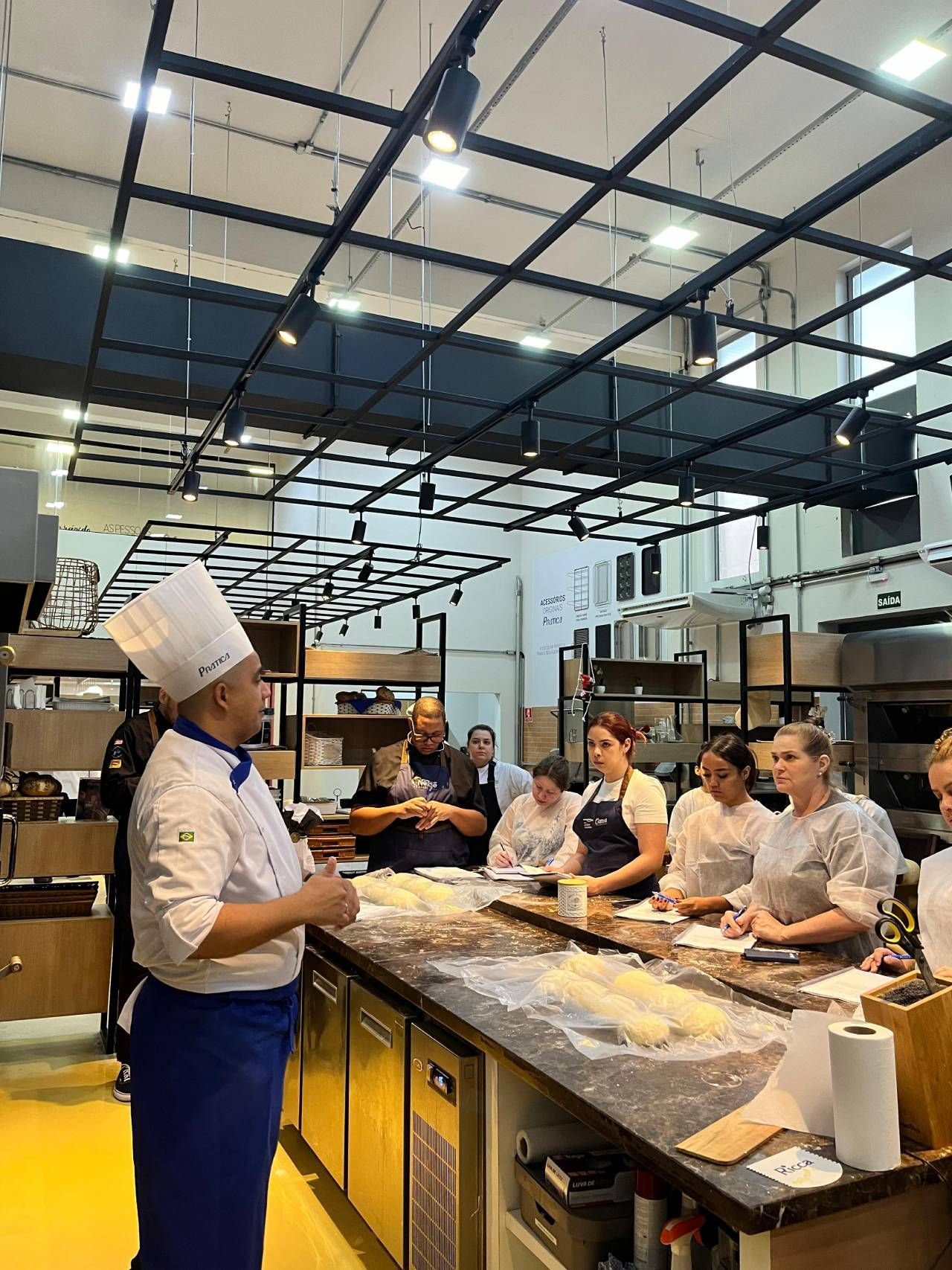 Um chef está em uma cozinha conversando com um grupo de pessoas.