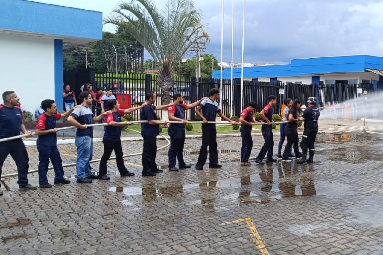 Bombeiros puxam uma mangueira e jogam água no pavimento de tijolos molhado perto de um prédio azul.