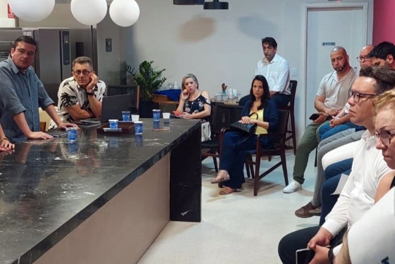 Um grupo de pessoas está sentado ao redor de uma mesa em uma sala.