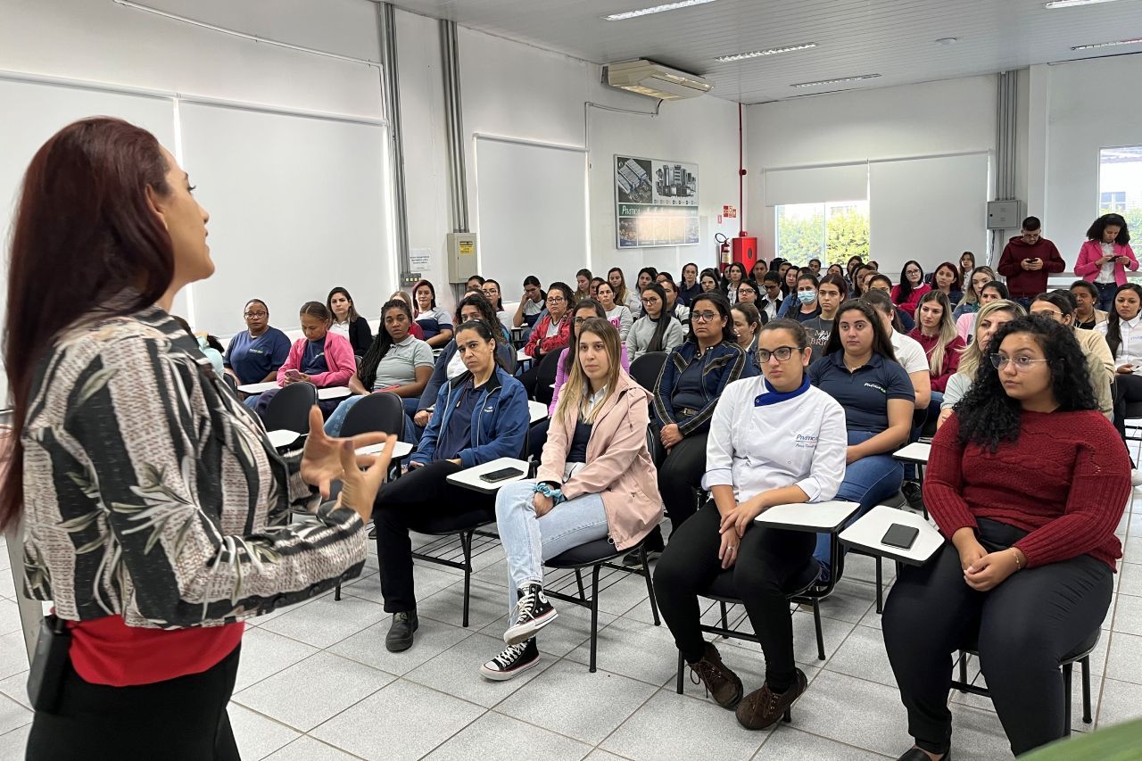 Uma mulher está parada na frente de um grande grupo de pessoas em uma sala de aula.