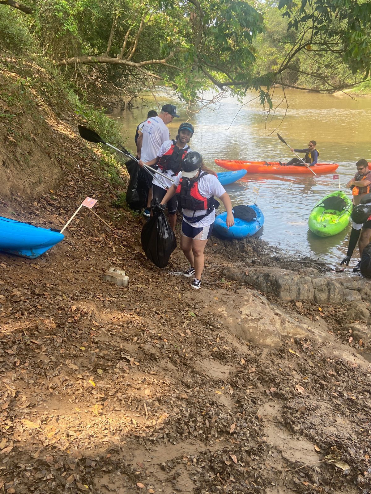 Um grupo de pessoas está de pé ao lado de caiaques na margem de um rio.