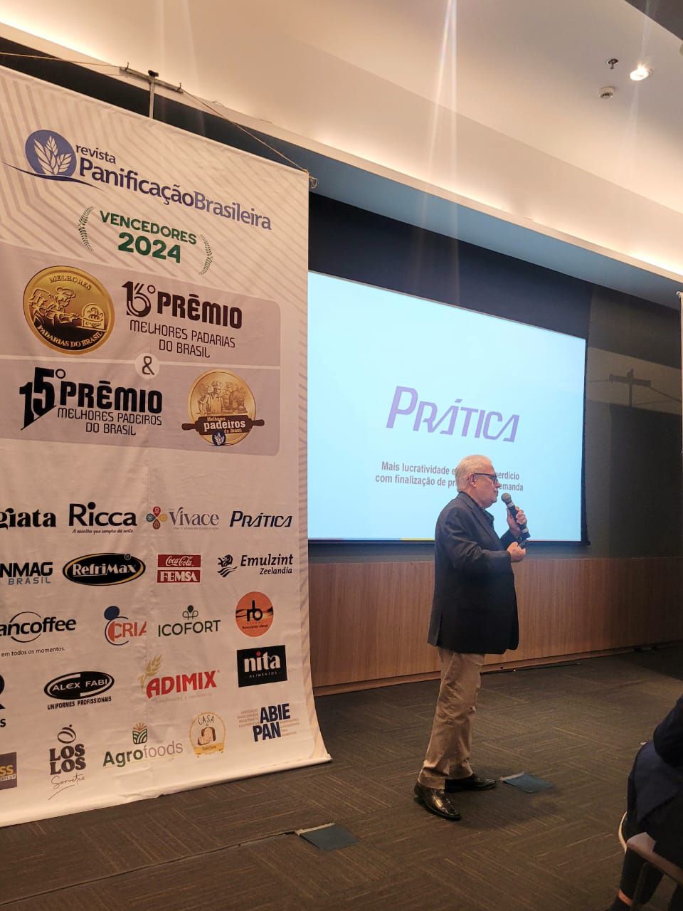 Um homem está fazendo uma apresentação em frente a uma tela grande.