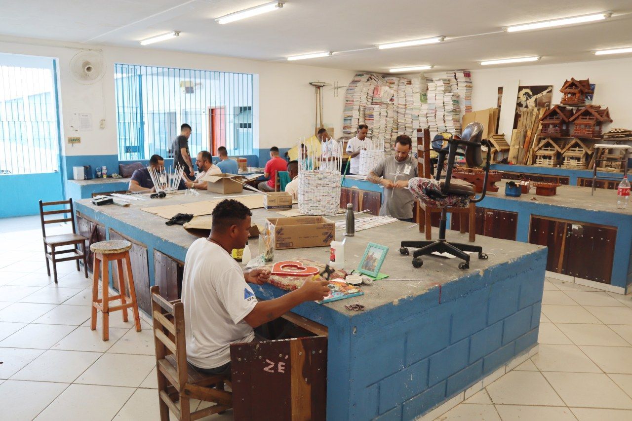 Um homem está sentado à mesa em uma sala com outras pessoas.