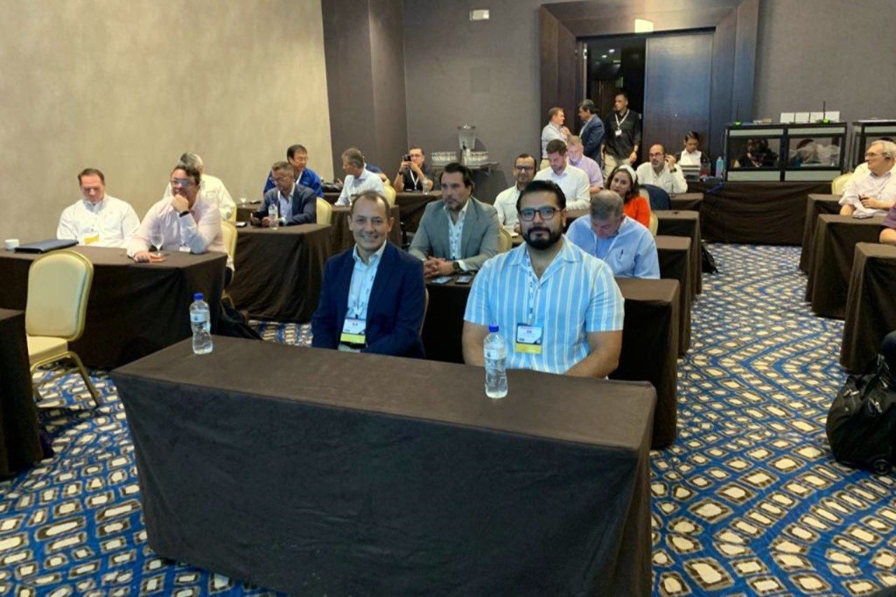 Um grupo de pessoas está sentado em mesas em uma sala de conferências.