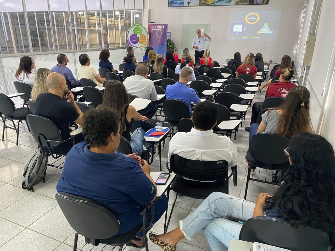 Um grupo de pessoas está sentado em uma sala de aula assistindo a uma apresentação.