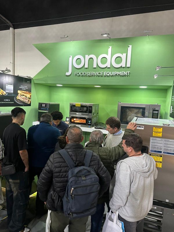 Um grupo de pessoas está em frente a uma exposição de equipamentos de alimentação da Jondal.