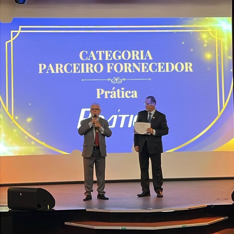 Dois homens estão em um palco em frente a uma tela que diz