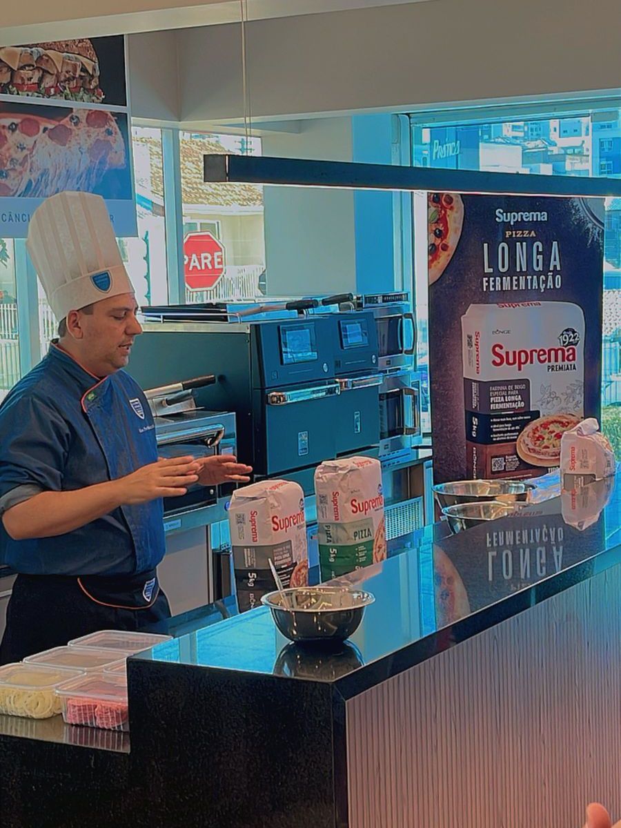 Um homem com chapéu de chef está em pé no balcão de um restaurante.