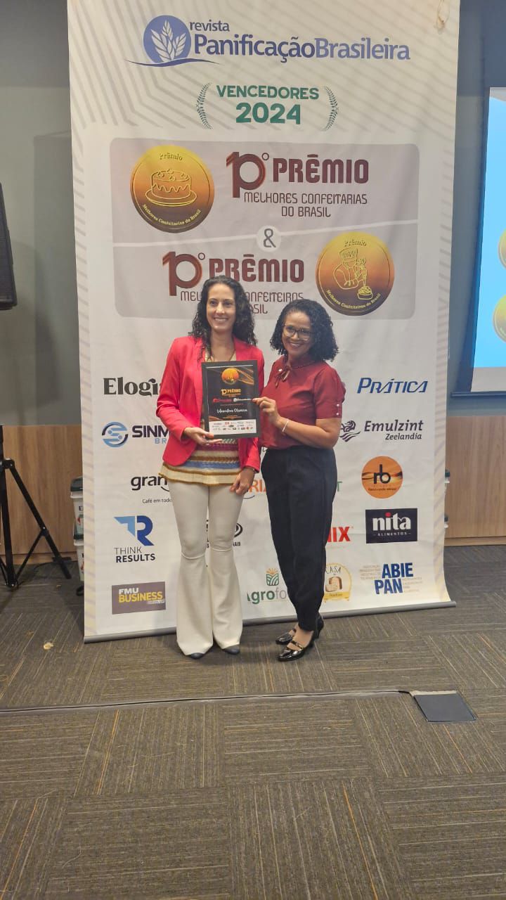 Duas mulheres estão de pé, uma ao lado da outra, em frente a uma faixa.