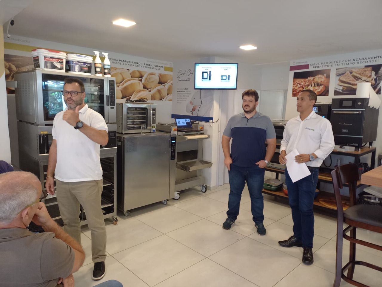 Um grupo de homens está em uma sala com uma TV na parede.