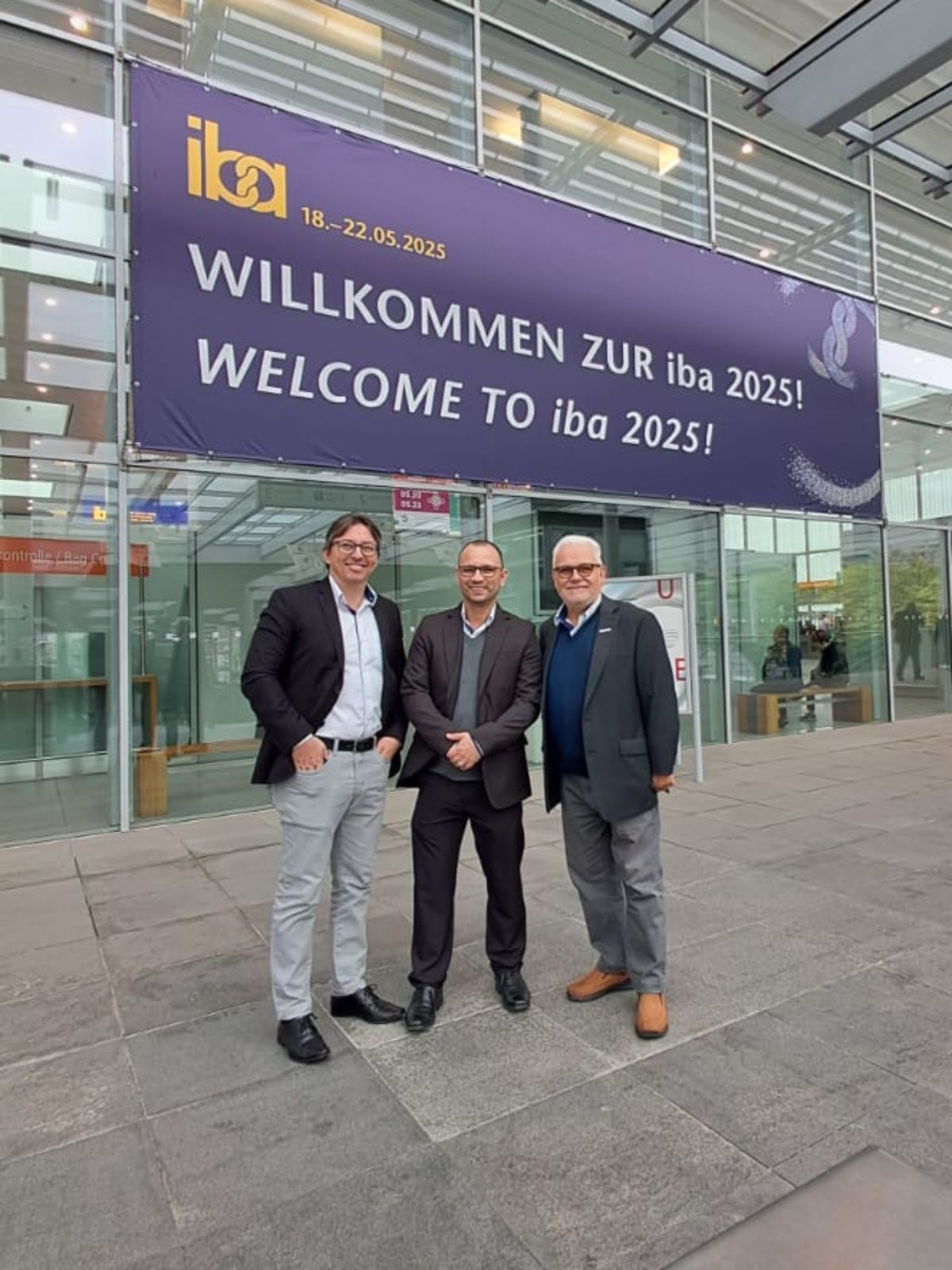 Três homens estão em frente a uma placa que diz bem-vindo à iba 2025.