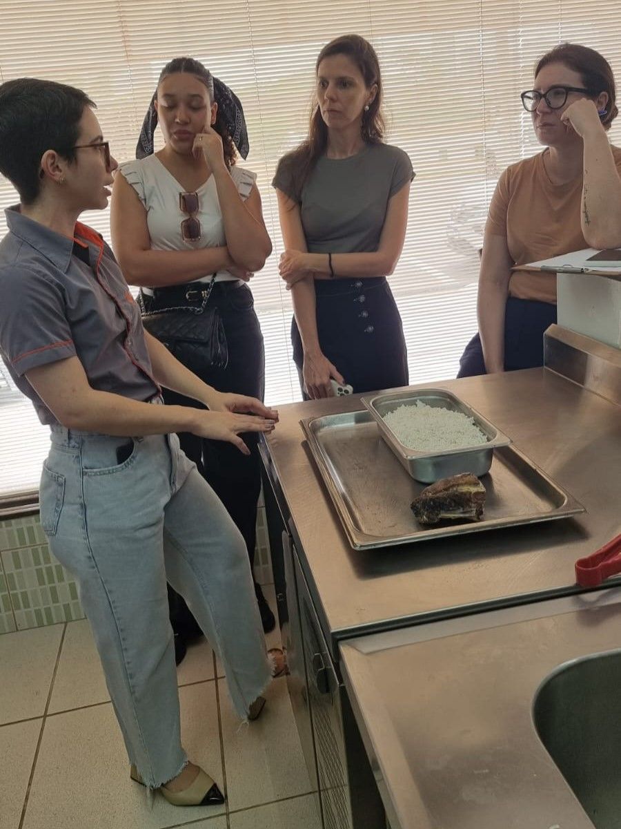 Um grupo de mulheres está de pé ao redor de uma mesa com uma bandeja de comida sobre ela.