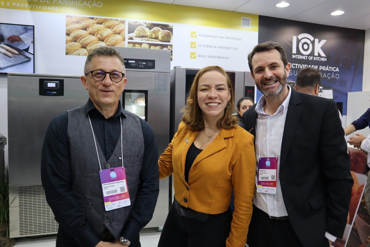 Três pessoas estão posando para uma foto em frente a uma geladeira.