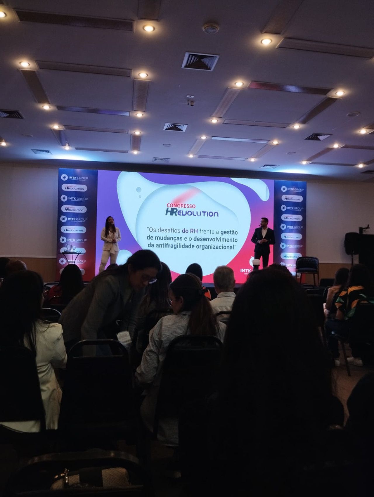 Um grupo de pessoas está sentado em uma sala grande assistindo a uma apresentação