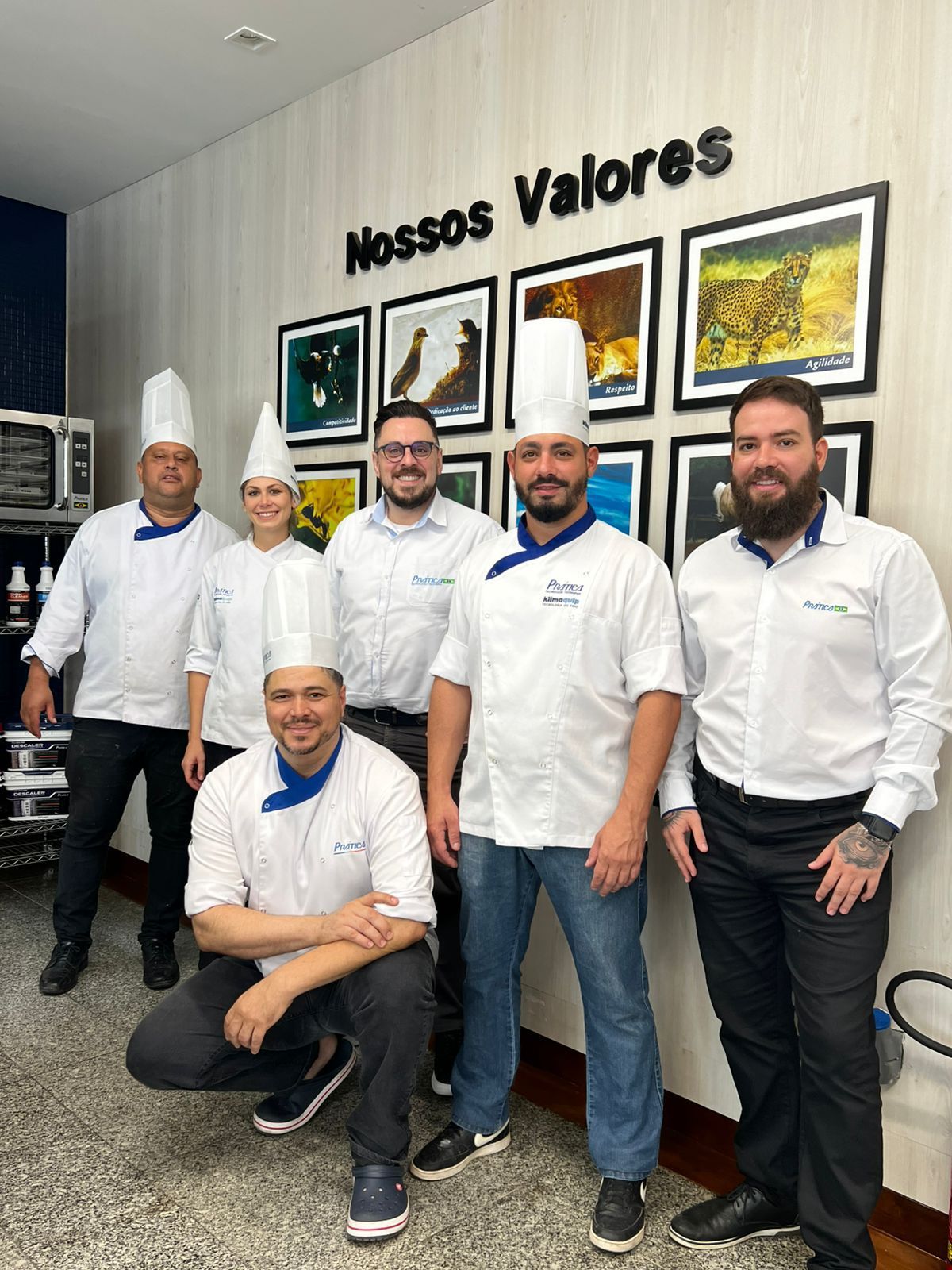 Um grupo de chefs está posando para uma foto em frente a uma parede com fotos.