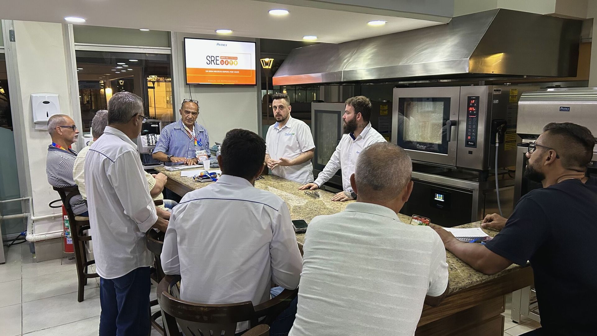 Um grupo de homens está sentado ao redor de uma mesa na cozinha.