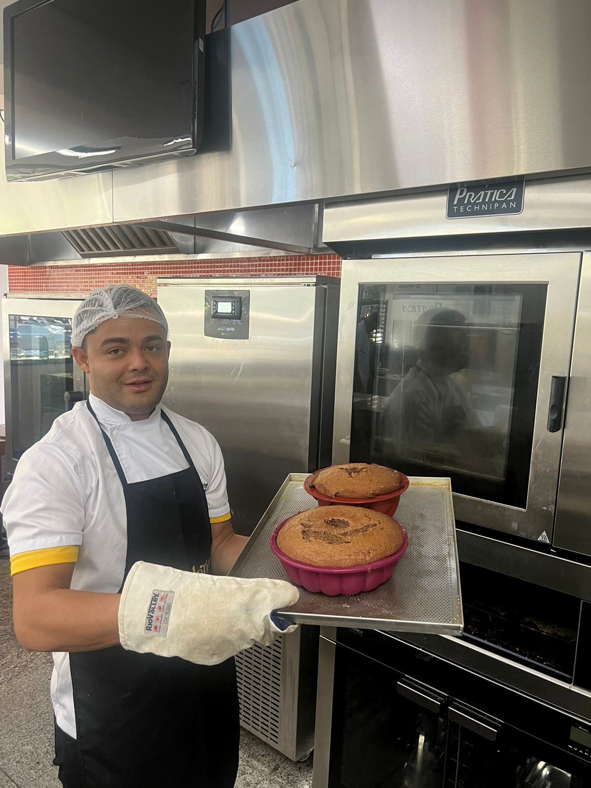 Um homem está segurando uma bandeja de bolos em frente ao forno.