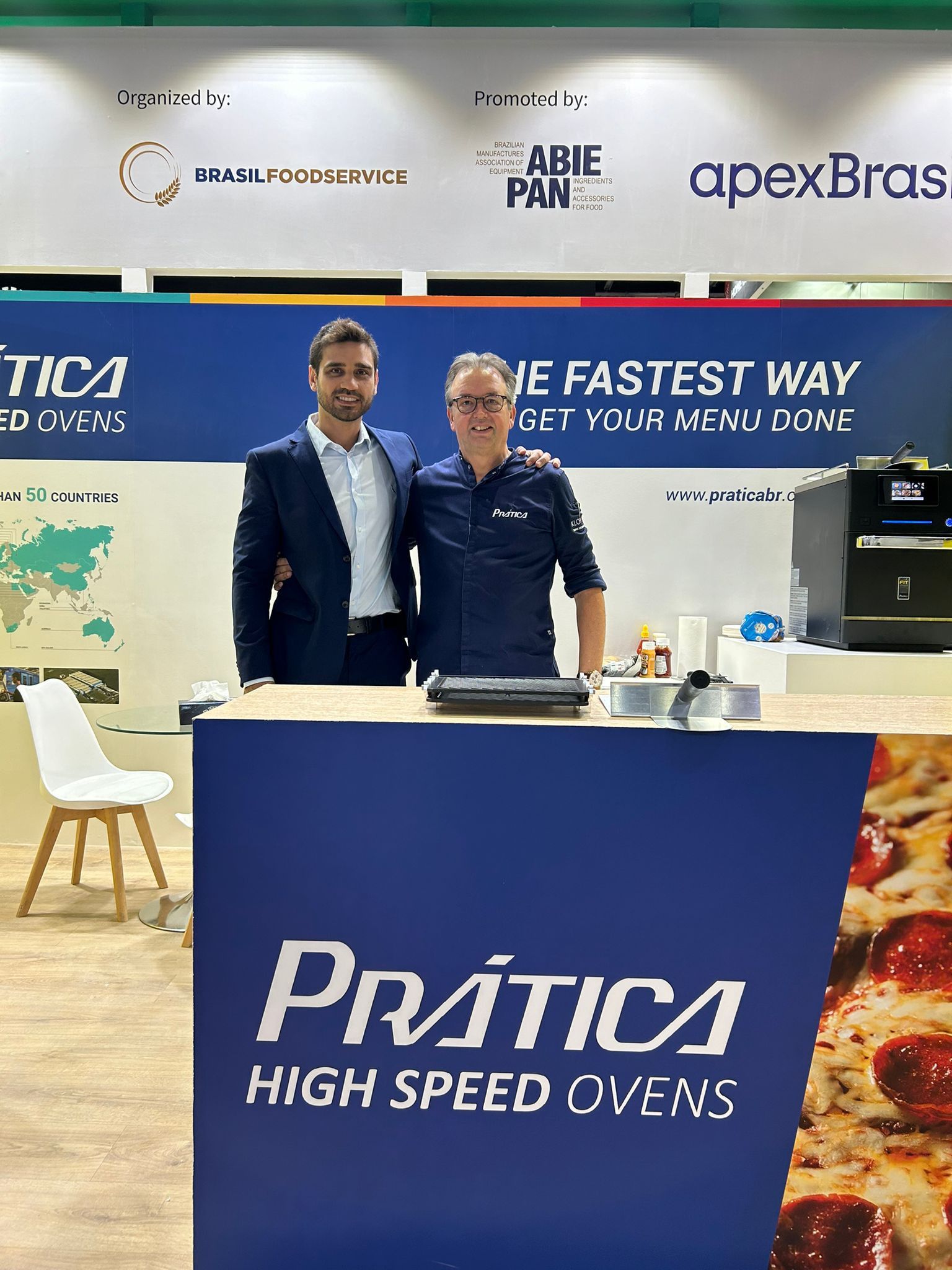 Dois homens posando para uma foto em frente a um forno de alta velocidade