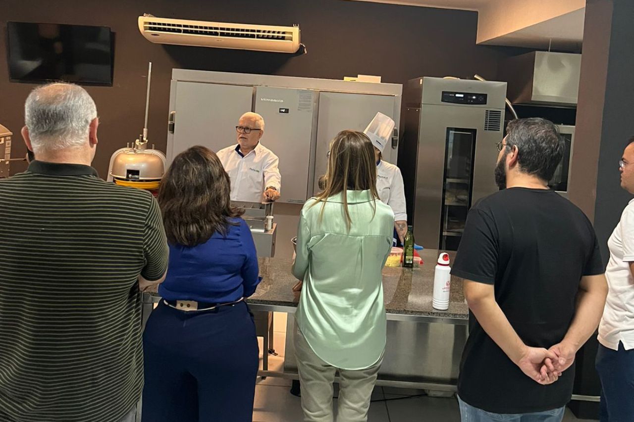 Um grupo de pessoas está em pé na frente de um chef em uma cozinha.