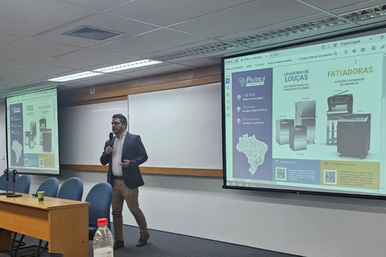 Um homem está fazendo uma apresentação em frente a uma tela grande em uma sala de conferências.