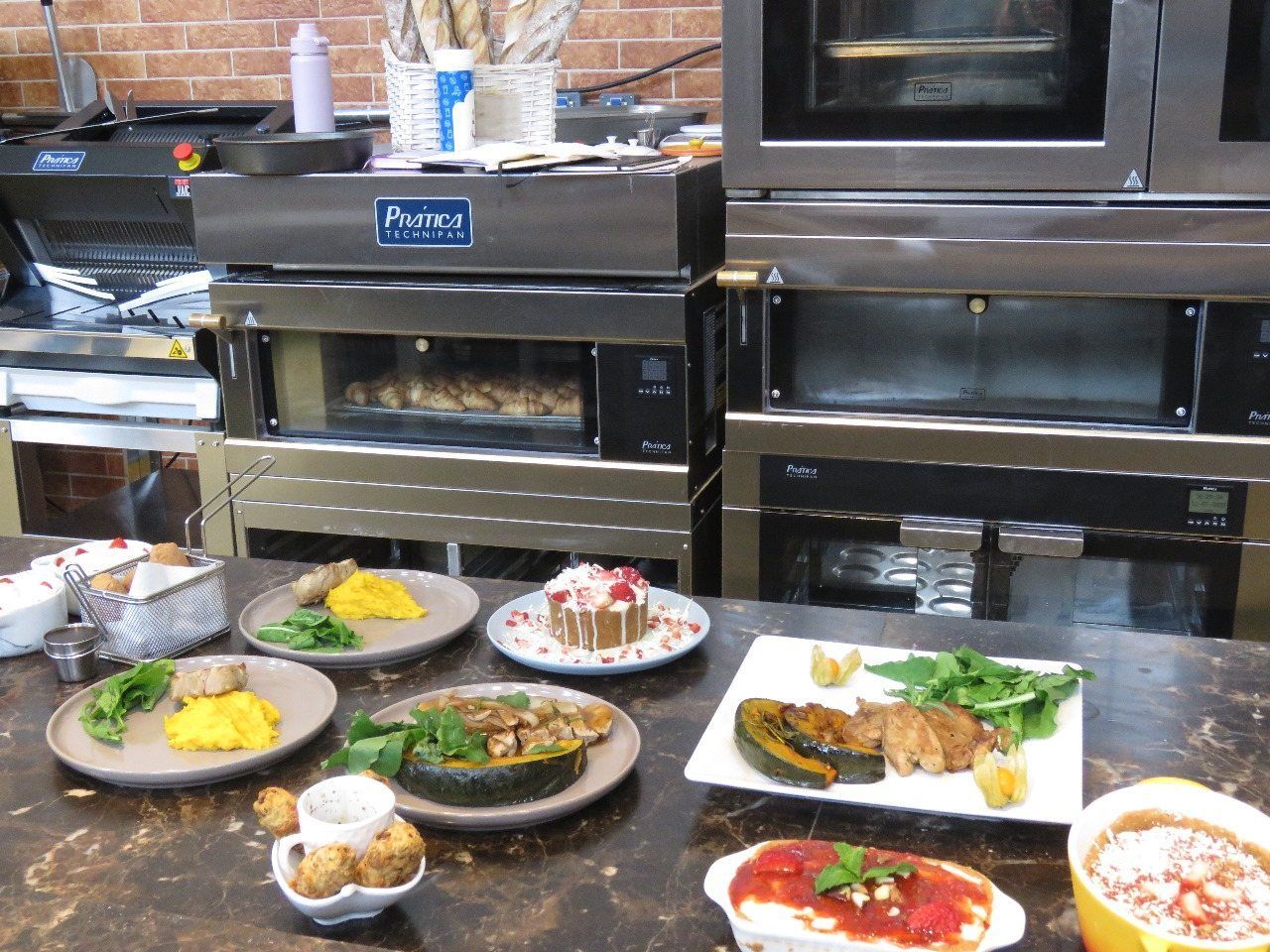 Vários pratos de comida estão em um balcão em frente a dois fornos.