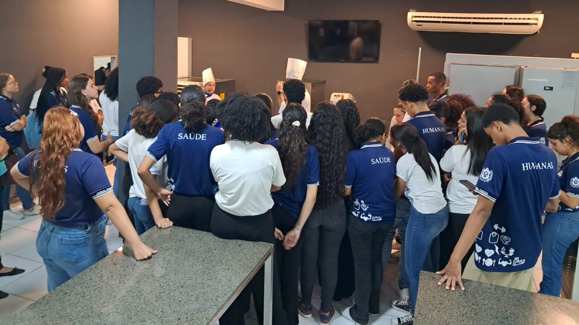 Um grupo de pessoas está em pé ao redor de um balcão na cozinha.