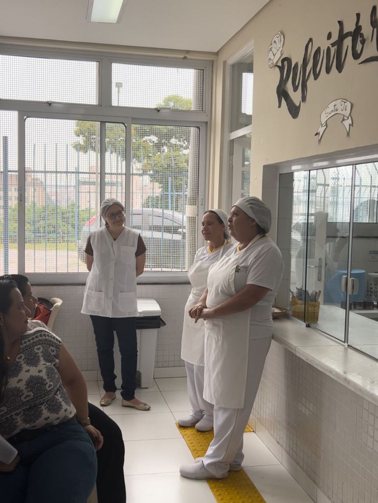 Um grupo de mulheres em aventais brancos estão de pé em uma sala.