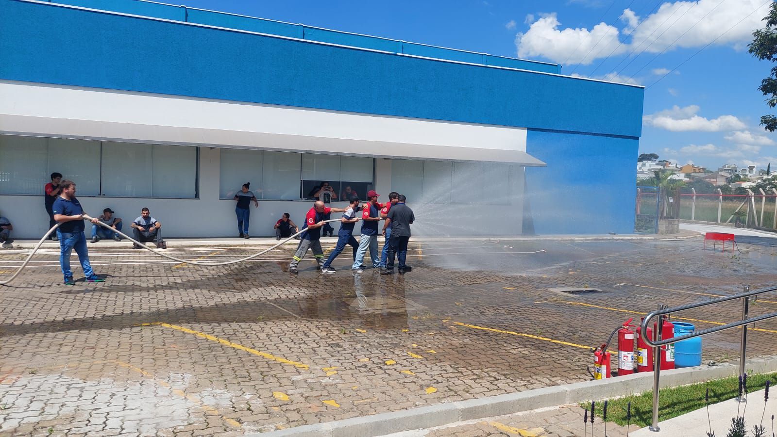 Um grupo de pessoas está em frente a um prédio jogando água no chão.