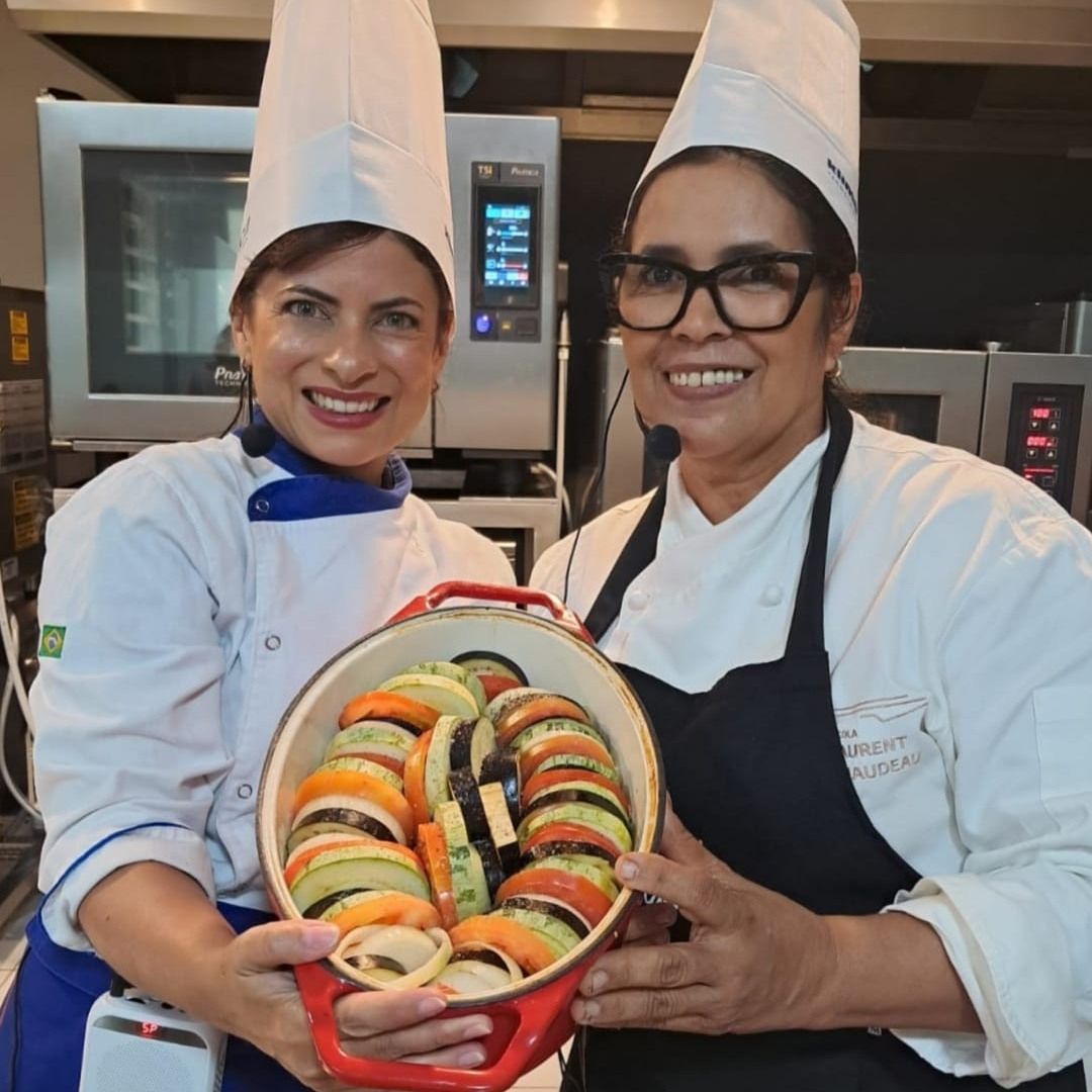 Duas mulheres com chapéus de chef seguram uma panela de vegetais