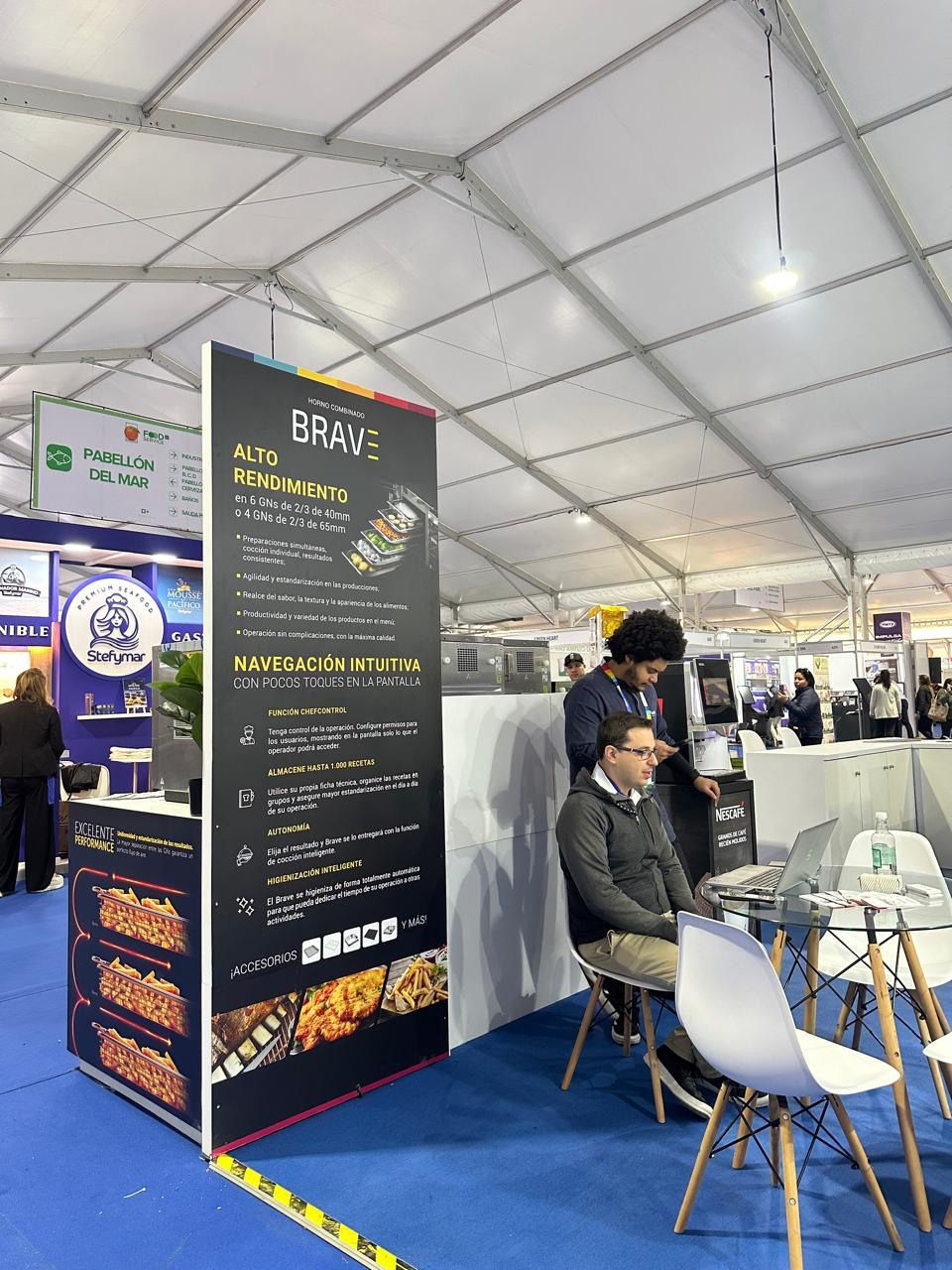 Um grupo de pessoas está sentado em mesas em uma tenda.