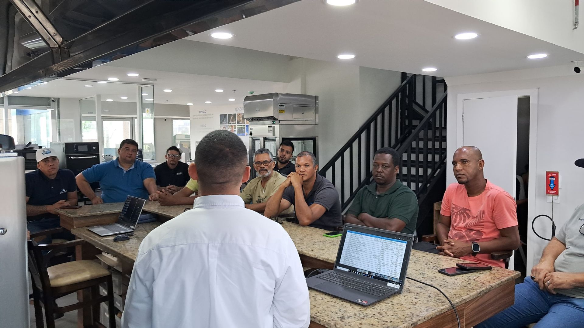 Um grupo de homens está sentado ao redor de uma mesa com laptops.
