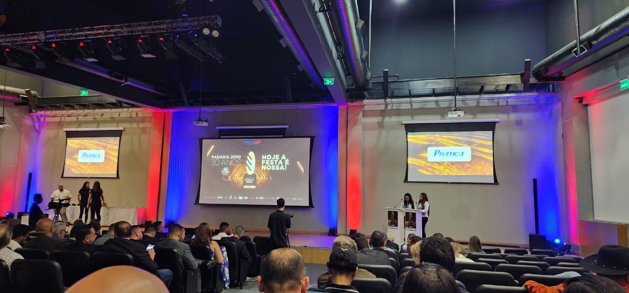 Um grande grupo de pessoas está sentado em um grande auditório assistindo a uma apresentação.