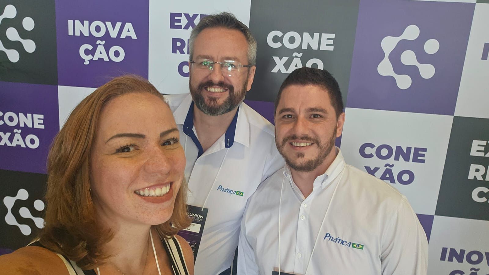 Uma mulher e dois homens estão posando para uma foto em frente a uma parede roxa.