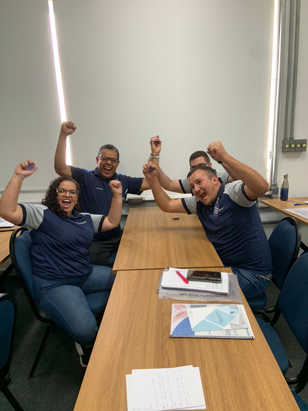 Um grupo de pessoas está sentado à mesa com os braços no ar.