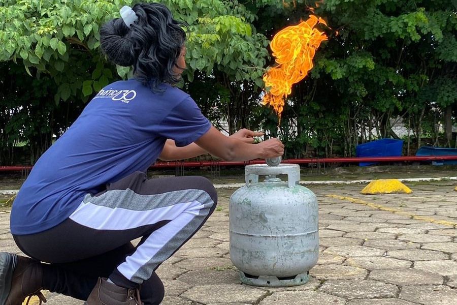 Uma mulher está ajoelhada ao lado de um cilindro de gás com chamas saindo dele.