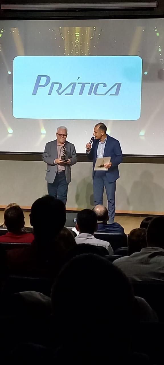Dois homens estão em pé diante de uma tela grande com a palavra pratica escrita nela.