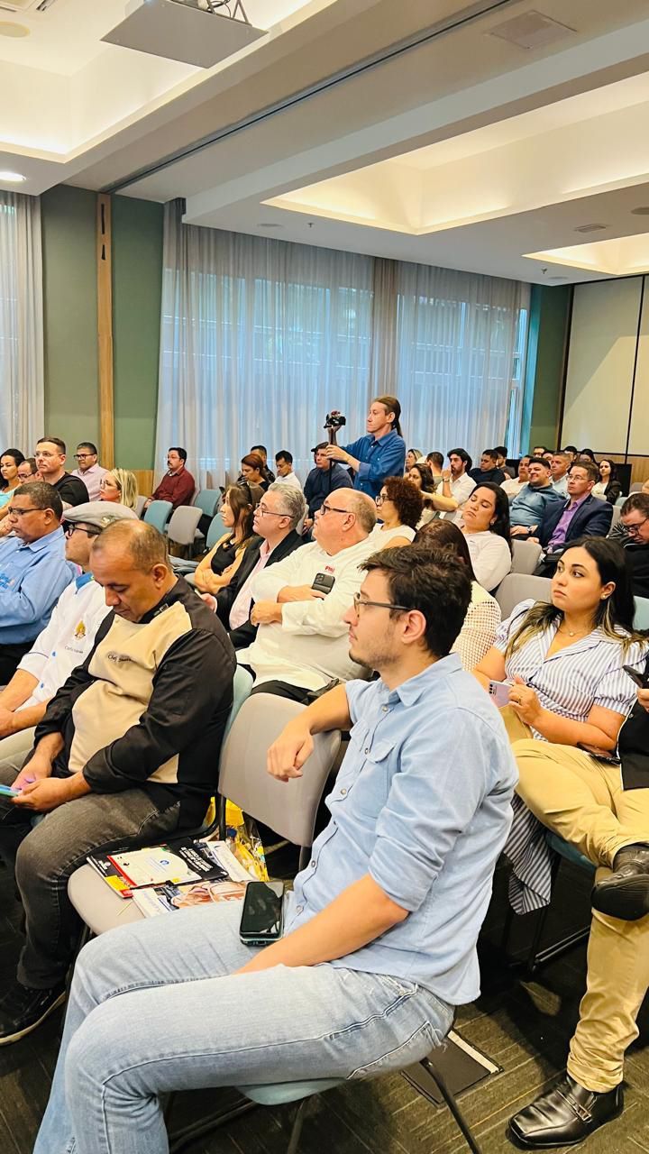 Um grande grupo de pessoas está sentado em cadeiras em uma sala.