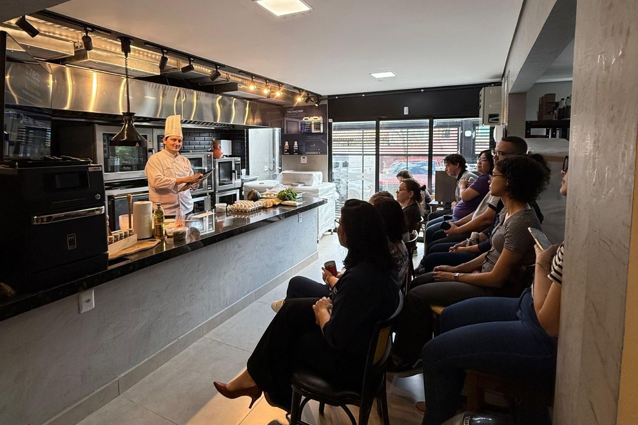 Chef fazendo demonstração culinária para uma plateia sentada na cozinha de um restaurante.