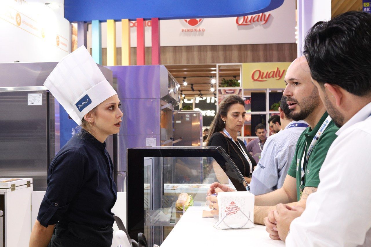 Uma mulher com chapéu de chef está conversando com um grupo de pessoas.