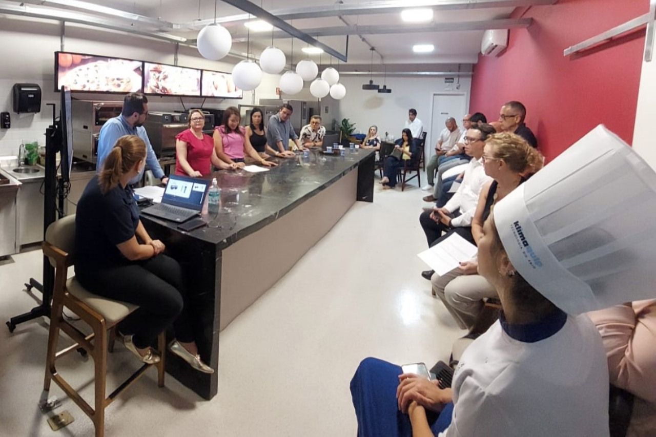 Um grupo de pessoas está sentado ao redor de uma longa mesa em uma cozinha