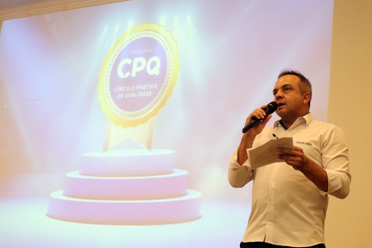 Um homem está segurando um microfone em frente a uma tela que diz cpq.