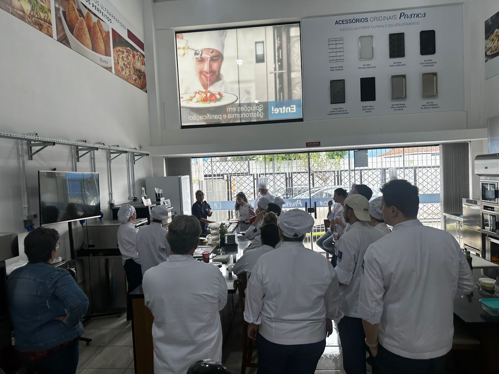 Um grupo de pessoas está em frente a uma tela grande com um chef nela.