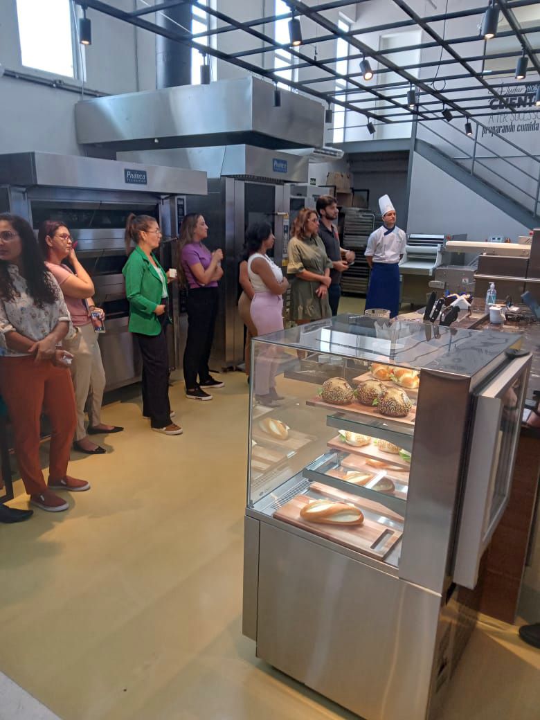 Um grupo de pessoas está em volta de uma vitrine em uma padaria.